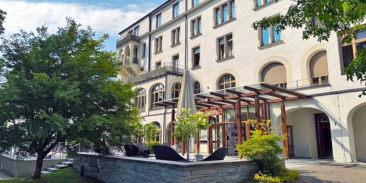 Das Bild zeigt die ruhige und einladende Außenansicht eines Hotels mit einem modernen Anbau an einem sonnigen Tag.