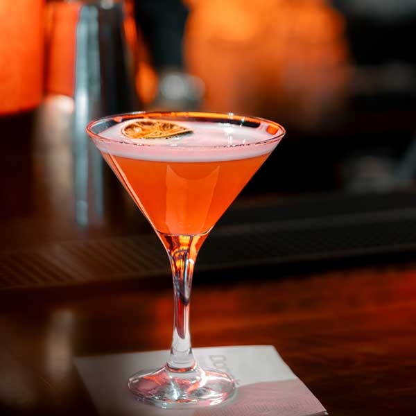 Das Bild zeigt einen köstlich aussehenden Cocktail in einer Martini-Glas auf einer Bar.